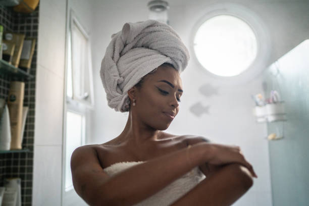 Young woman applying moisturizer on the body after shower at home